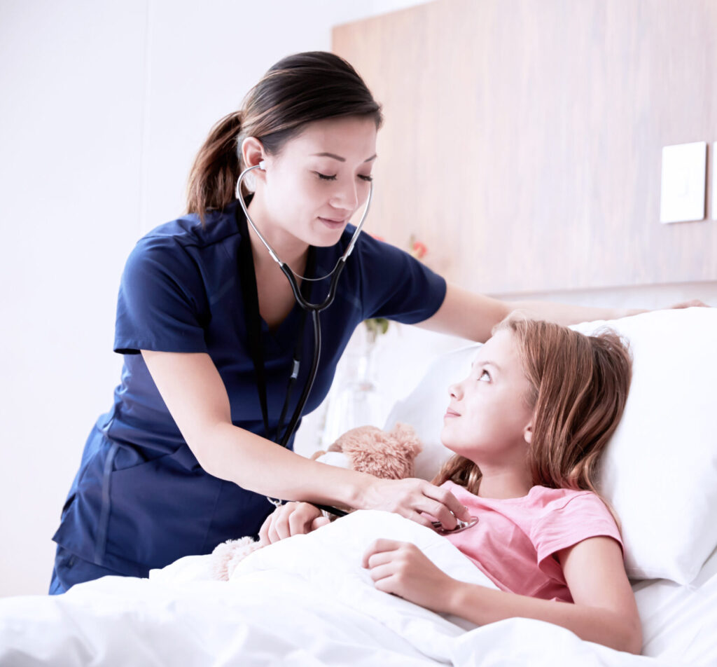 Female Vocational Nurse Examining Girl Lying In Hospital Bed Hugging Teddy Bear